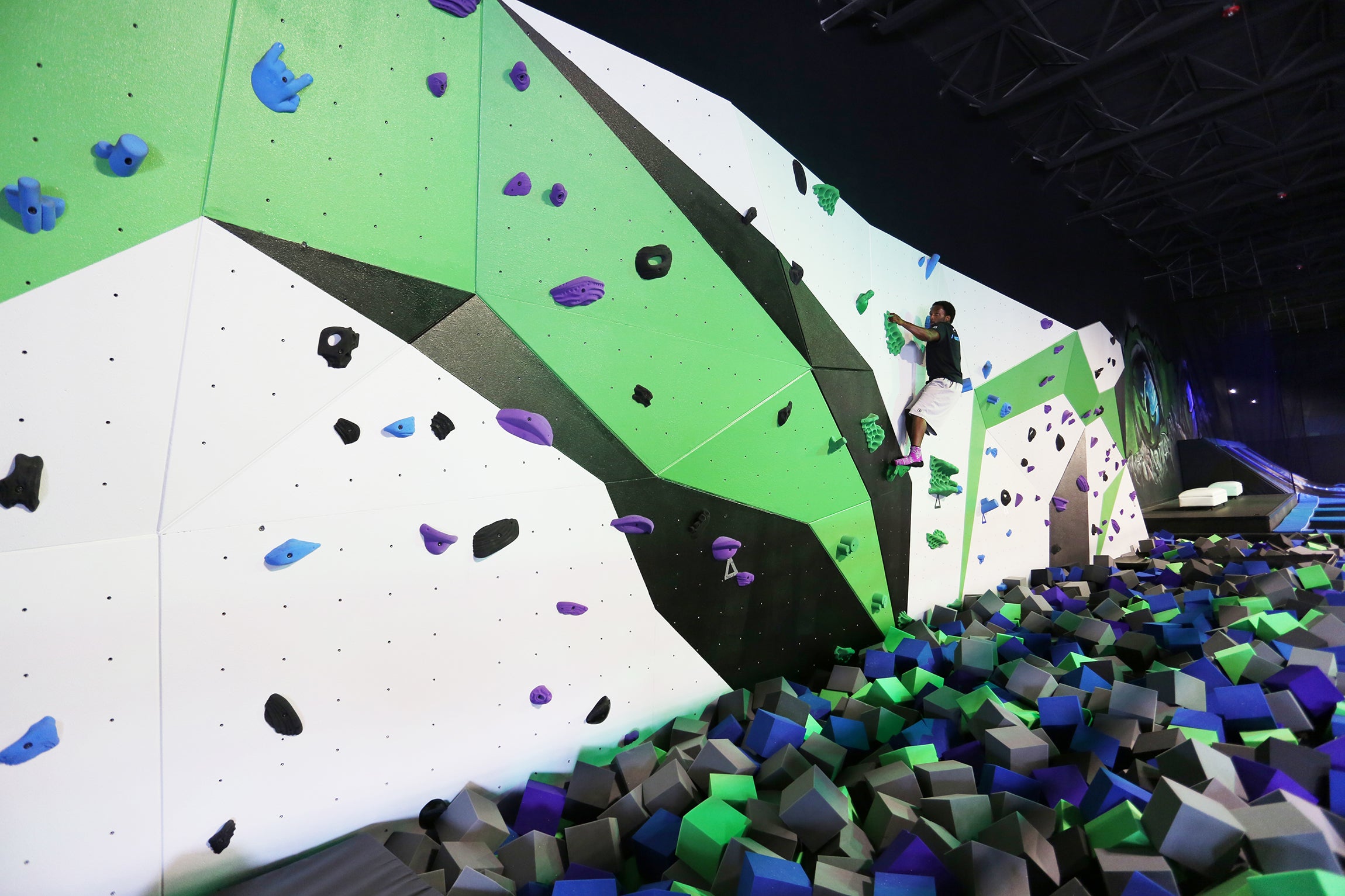 Man tries sport climbing on a bouldering wall in a trampoline park