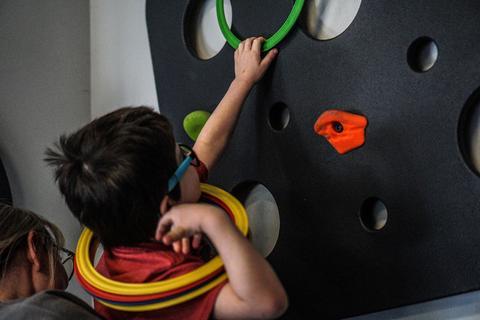 child uses rings on a climbing wall in a pediatric occupational therapy office